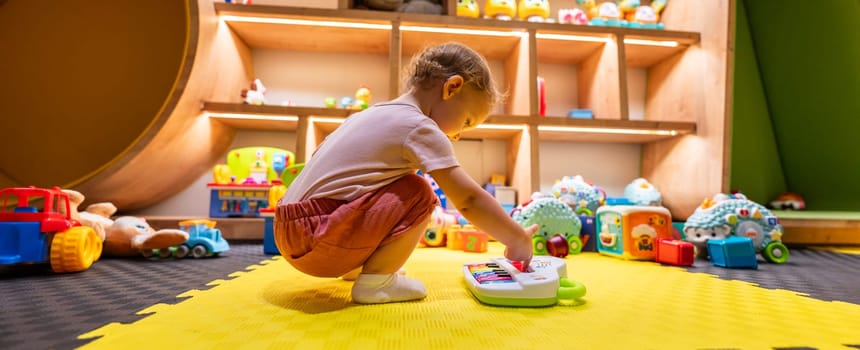 Toddler playing with colorful musical toy piano in a bright playroom filled with educational toys and activities for early childhood development