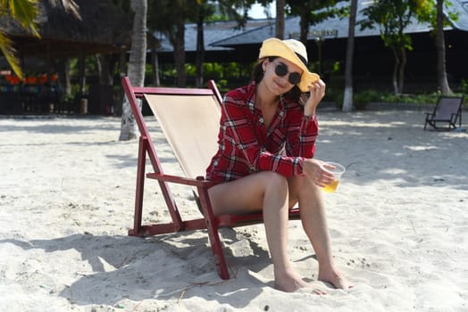 Young woman in hat sitting on the desk chair at the beach with white sand in Vietnam