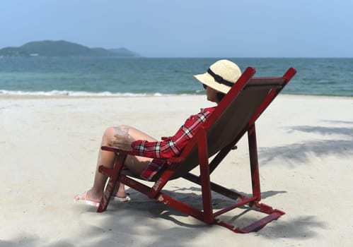 Young woman in hat sitting on the desk chair at the beach with white sand in Vietnam