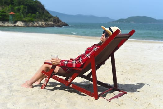 Young woman in hat sitting on the desk chair at the beach with white sand in Vietnam