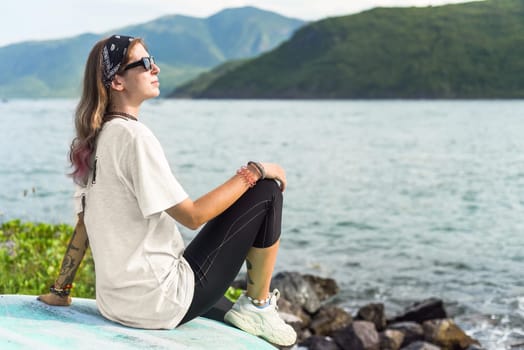 Young travel woman sitting with sunglasses and bandana on the shore of south china sea in vietnam