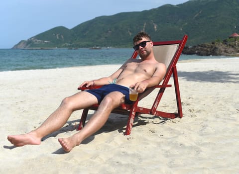 Young man drinking beer and sitting on deck chair at beach in Nha Trang