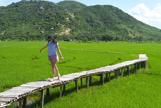 A young woman walking across wooden pier in a rice field