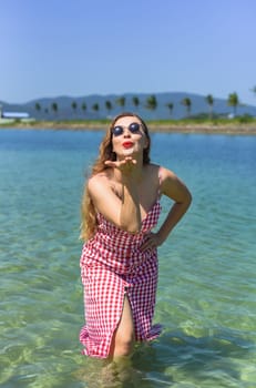 Bright blond young woman standing in sea and sending air kiss