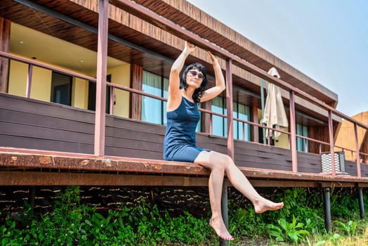 50 years old russian woman in short dress and sunglasses sitting on a balcony and enjoying on the summer day