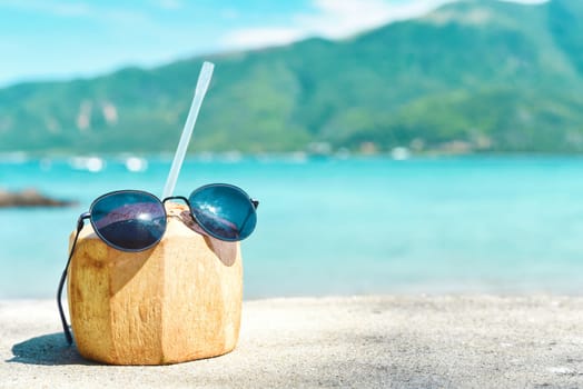 Coconut drink with straw and sunglasses on tropical beach background