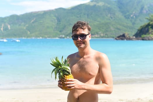 Young man holding a pineapple on sandy beach in Vietnam
