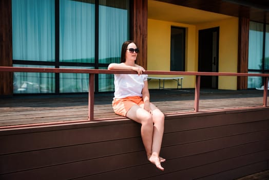36 years old russian woman in orange shorts and sunglasses sitting on a balcony and enjoying on the summer day