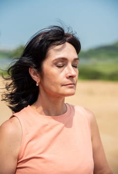 portrait of 50 years old russian woman in and peach fuzz color shirt with eyes closed enjoyng the weather on the summer day