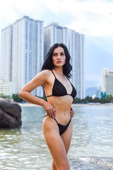 Slender sexy ukrainian 37 years old woman in black bikini standing again stones in the water and holding her hair