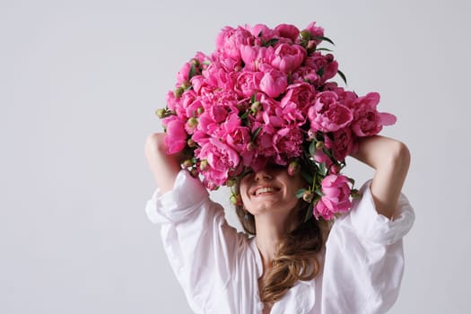 happy woman covering her face with a bouquet of peonies on a white background,