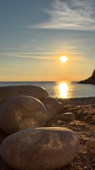 Smooth boulders on the beach, the sun sets over the calm waters, a warm reflection reflects in the sea. High quality photos