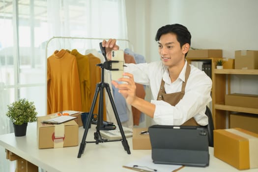 Young retailer adjusting smartphone on tripod for live streaming product to an online audience.
