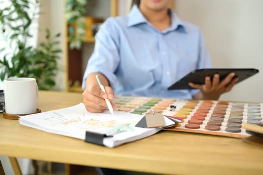 Interior designer selecting color samples while sketching design ideas on paper..
