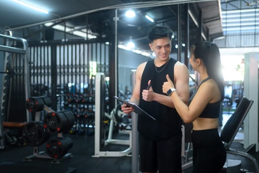 Fitness trainer and a female client sitting on the gym floor discussing progress and workout plans.