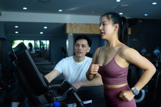 Young woman jogging on treadmill while her trainer monitors her progress and provides guidance.
