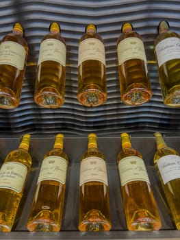 A collection of Sauternes wine bottles showcases their golden color and intricate labels, arranged on sleek shelving in a contemporary wine cellar, ideal for enthusiasts and collectors.