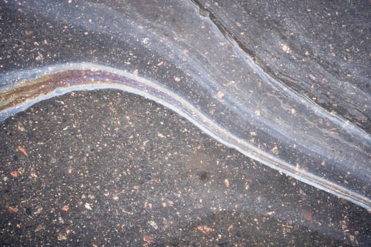 Brightly colored patterns appear on the asphalt due to an oil slick, highlighting the aftermath of rain in an urban area.