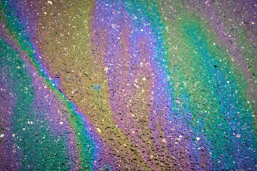 Colorful gasoline spill creating a rainbow effect on asphalt road surface.
