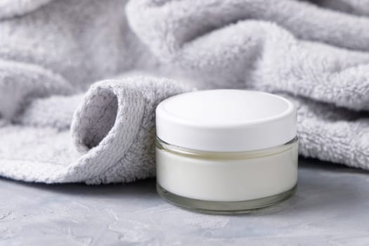 Cream jar with white lid near light gray bath towel closeup. Natural organic cosmetics for facial care. Lifestile scene of skincare, essence of Spa and Wellness, macro cream texture