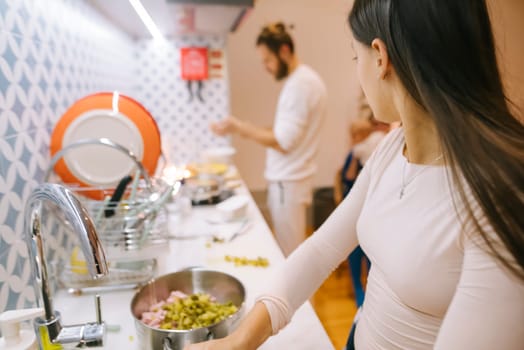 In a modern kitchen, a woman prepares colorful ingredients while a man cooks happily in the background