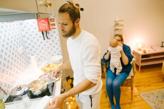 In a tranquil and serene family moment, dad is busy cooking while mom holds their adorable baby lovingly close