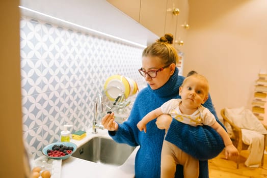 A loving mother gently cradles her baby in her arms, all while she prepares delicious food in a modern kitchen