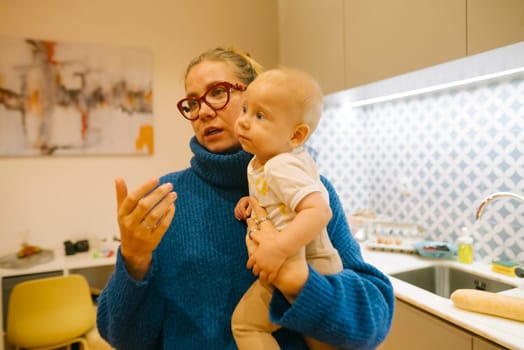 A loving mother holds her adorable baby while having a warm conversation in a stylish, contemporary kitchen environment