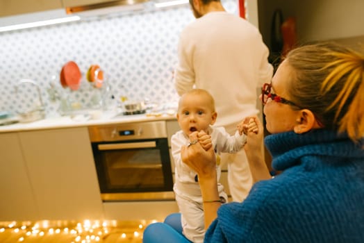 A heartwarming scene of a cute baby practicing walking with family members in a lovely modern kitchen
