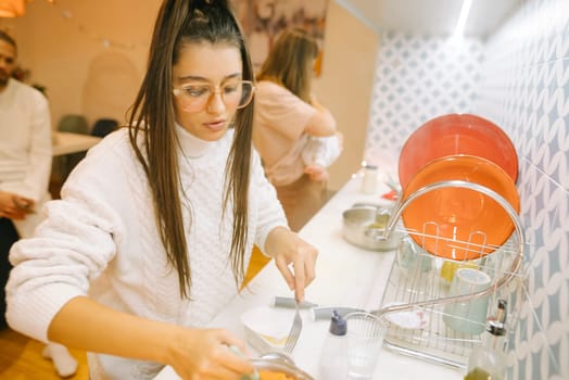 A focused young woman skillfully washes dishes in a stylish kitchen, fully embodying the essence of modern home life