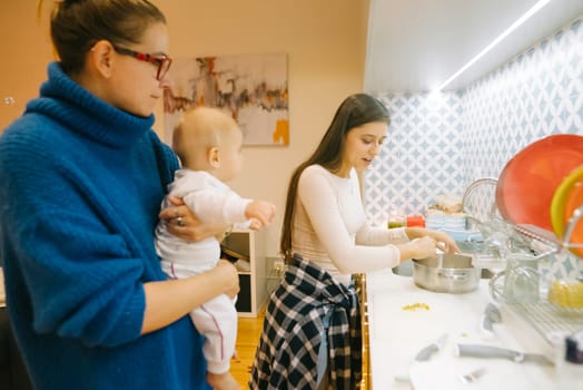 A warm and inviting cozy kitchen scene showcasing a mother cooking with her baby and daughter together