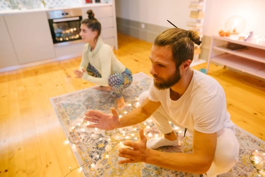 A couple is peacefully meditating and practicing yoga in a warm, inviting room beautifully decorated with lovely lights