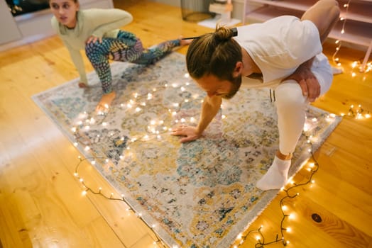 A couple participates in a relaxing yoga session on a beautiful rug that is surrounded by soft, warm lights