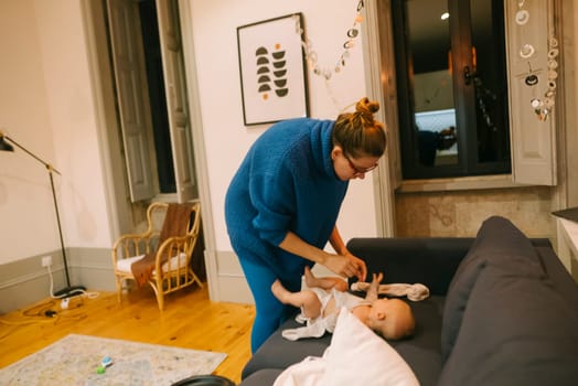 In a stylish, cozy living room filled with vibrant decor, a mother lovingly and gently changes her babys diaper