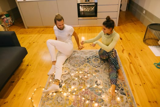 A couple joyfully shares a cherished moment on a plush rug, beautifully surrounded by cozy warm fairy lights