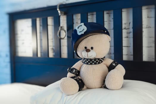 A toy teddy bear dressed in leather straps is a BDSM accessory for adult games in a police hat on the bed