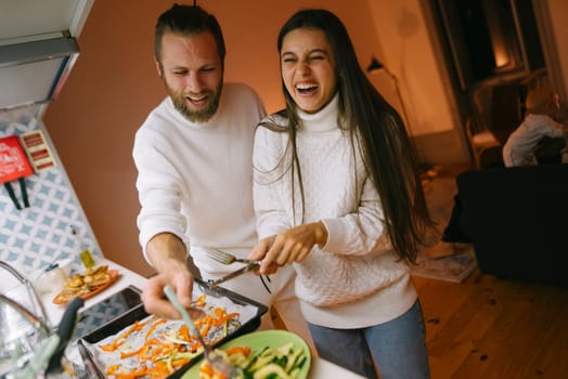 In a warm and cozy kitchen, a joyful couple engages in cooking together, sharing laughter and creative culinary moments