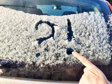 A car's rear windshield is covered in snow and frost, displaying a question mark drawn with a finger, indicating uncertainty.