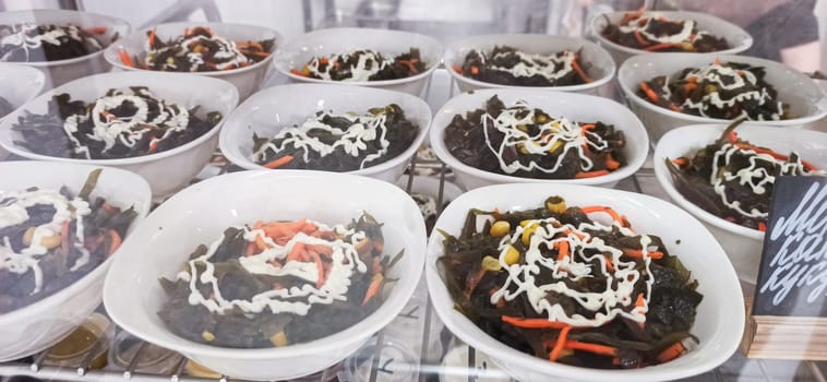 Various salad bowls filled with leafy greens, mixed vegetables, and topped with a swirl of creamy dressing are neatly arranged for customers to admire. The vibrant colors entice passersby.