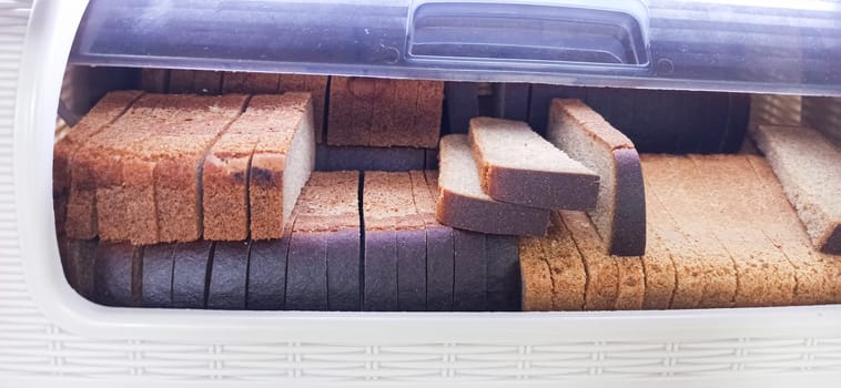 A variety of sliced bread neatly arranged in a white bread box. The bread includes whole wheat, rye, and traditional white options. This setup ensures freshness and convenience.