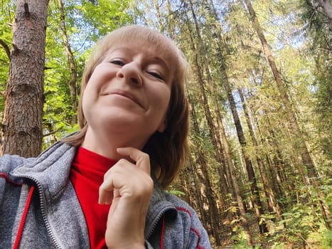 A middle-aged woman enjoys a delightful moment in a tranquil forest, capturing her smile while exploring nature.