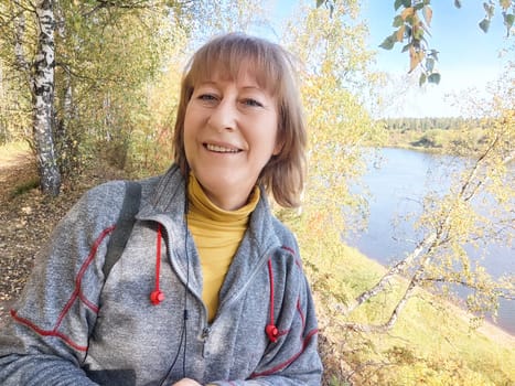 Woman smiling happily while exploring a scenic riverside in autumn, surrounded by colorful foliage and nature's beauty.