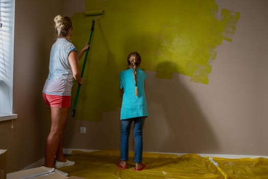 A joyful family moment as a child and adult paint a wall together, showcasing creativity and teamwork.