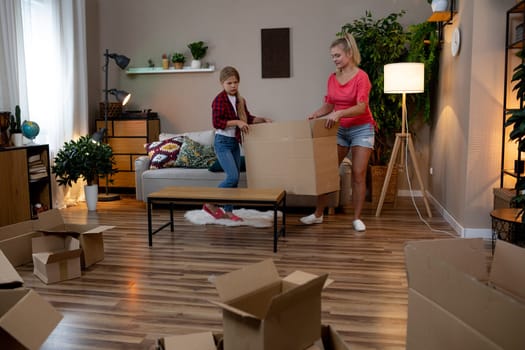 A joyful mother and her enthusiastic child are happily unpacking several boxes in their bright and cheerful living room