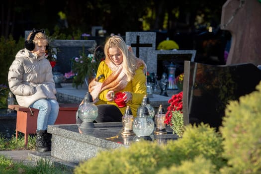 Two women sit quietly together at a serene cemetery, honoring cherished memories with beautiful flowers and candles