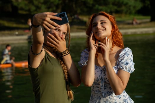 Two joyful friends are happily enjoying capturing a fun selfie together at the serene lake on a beautiful sunny day