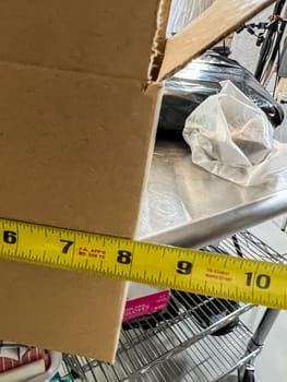 Castle Rock, Colorado, USA-July 28, 2023-A close-up view of a measuring tape stretched across a cardboard box to check its dimensions The tape measure shows a length of approximately 12 inches The box is placed on a reflective metal surface with other packaging materials nearby A close-up view of a measuring tape stretched across a cardboard box to check its dimensions The tape measure shows a length of approximately 12 inches The box is placed on a reflective metal surface with other packaging materials nearby