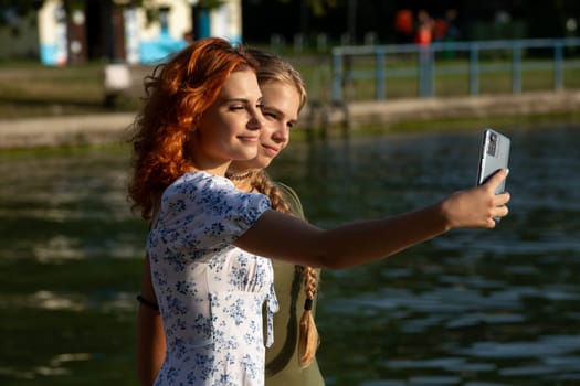 Two young women happily taking a selfie together by the serene lake, capturing a joyful moment in nature