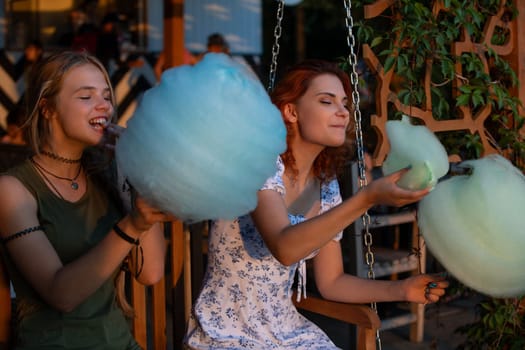 Two friends joyfully savoring fluffy cotton candy in a peaceful outdoor setting during the beautiful golden hour