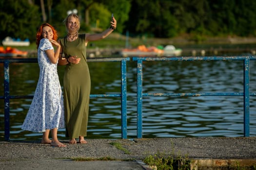 Two close friends joyfully pose by a serene lake, embracing cheerful summer vibes and enjoying their time together